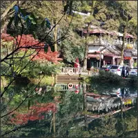 A traditional pavilion and brilliant red autumn trees reflected in a still pond.