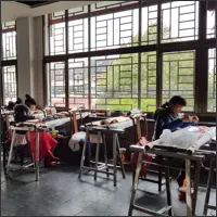 Several Xiang embroidery artisans work at individual frames beside the large windows of a shared studio.
