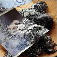 Bundles of fine grey, black and white silk threads lie across a paper embroidery design.