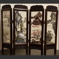 A small four-panel folding screen displays delicate embroidered mountain scenes in dark wooden frames.