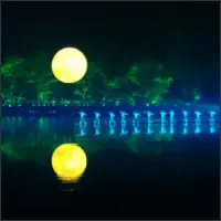Illuminated full moon and its reflection above performers on the dark lake.