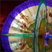 Performers and projected figures framed by a large circular folding fan.