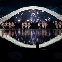 Ballet dancers beneath a sweeping white arch reflected in the water.