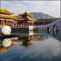 Arched stone bridge and Chinese pavilions reflected in calm water