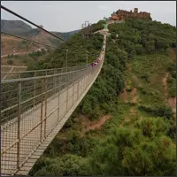 Long suspension bridge stretching across a valley toward a hilltop structure.