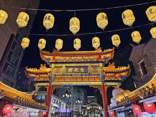 Illuminated traditional Chinese gate at night with two strings of glowing red lanterns.