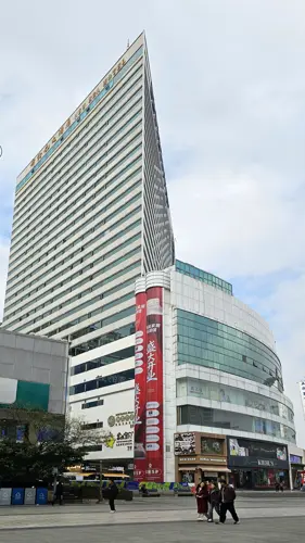 Angled view of the New Era Hotel in Kunming revealing its three-dimensional form, with the building tapering strongly toward one edge.