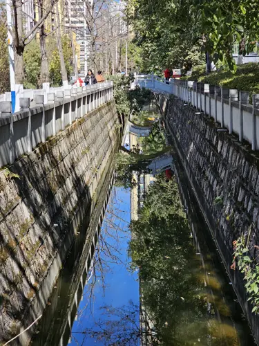 Clean canal-like section of the Panlong River with stone side walls, reflecting deep blue sky and surrounding vegetation in still water.