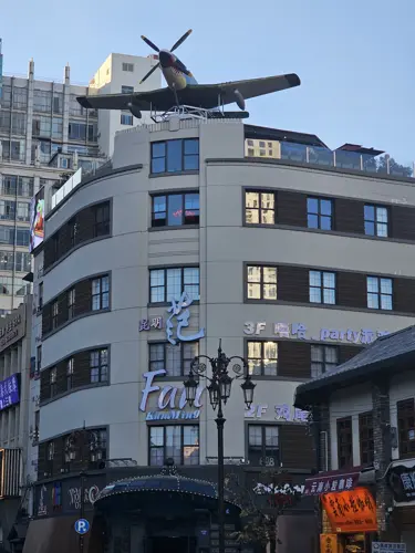 Rounded modern building in Kunming with a vintage aircraft mounted on the roof, referencing the city’s World War II aviation history, photographed in an urban street setting.