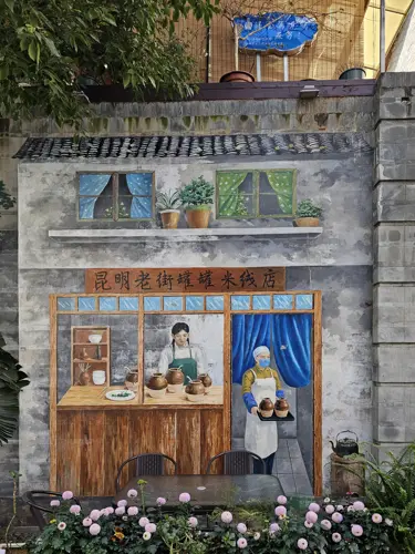 Wall mural in Kunming depicting a traditional clay-pot rice noodle shop, showing two cooks behind a wooden counter with jars, shelves, and a painted shop sign.