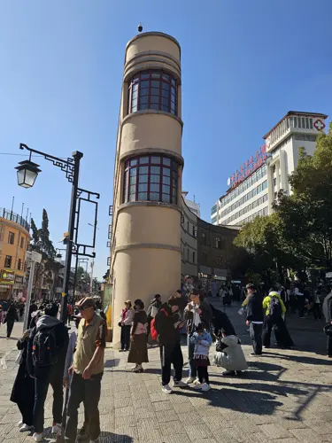 Modern curved high-rise in Kunming nicknamed the wine cup building, showing its rounded façade widening behind the front edge, with pedestrians and open plaza in sunlight.