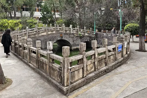 Small arched stone bridge enclosed within a square stone balustrade structure over green water at Wenmiao.