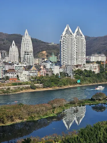 Daytime view of Jinghong skyline across the Lancang River with modern high-rise buildings and reflections in the water