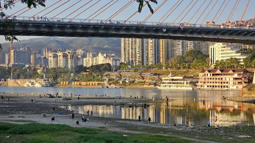 Closer view of Jinghong Lancang River Bridge with reflections in the water and people walking and gathering along the riverbank