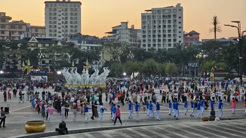Large group of people dancing and exercising together in a public square in Jinghong at sunset