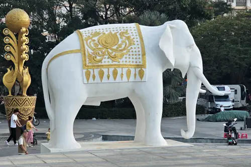 Large white elephant statue with gold decorations in a public square in Jinghong