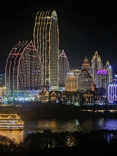 Night view of illuminated buildings in Jinghong reflected in the Lancang River with colorful city lights