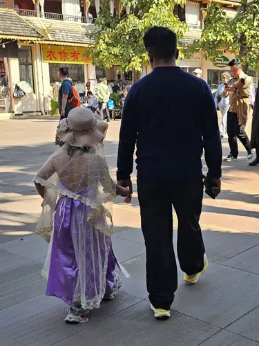 Adult and child walking hand in hand wearing colorful traditional-style outfits in Jinghong
