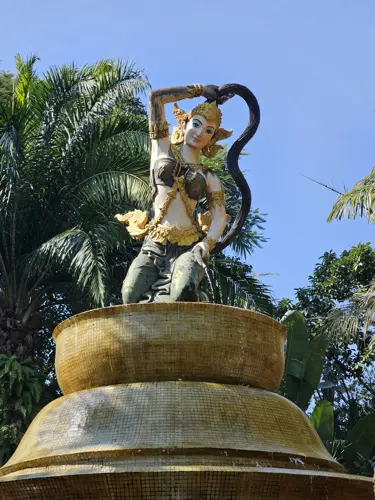 Decorative statue of a dancer figure on a pedestal surrounded by palm trees in Manting Park