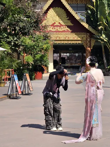 Photographer taking pictures of a person dressed in a traditional-style outfit in a public square in Jinghong