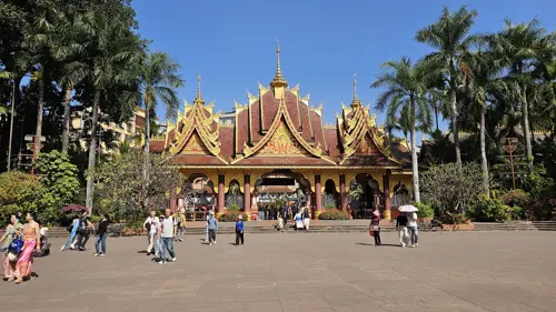 Entrance area of Manting Park in Jinghong with traditional Dai-style buildings and people walking across a wide plaza