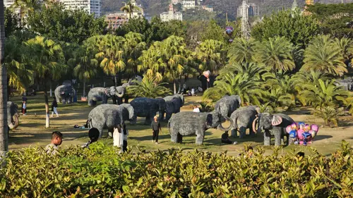 Group of elephant statues displayed in a landscaped park with palm trees in Jinghong