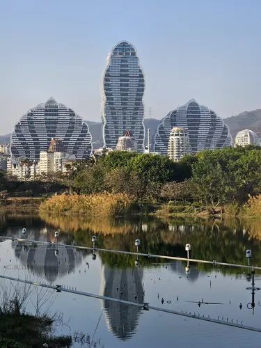 Curved modern buildings in Jinghong across the Lancang River with calm water and reflections in daylight