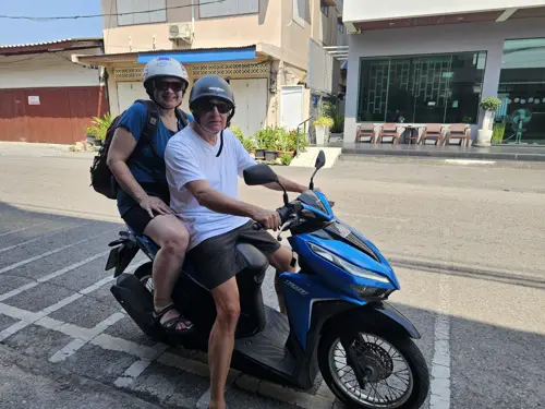 Two riders on a blue motorbike, ready to set off on a sunny street.