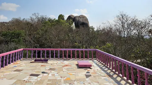 View from a mosaic-tiled platform with three massive boulders rising above the trees at Wat Khao Hin Thoen