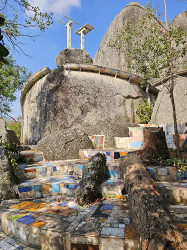 Mosaic steps leading up to a large boulder with small solar panels and a wind turbine on top
